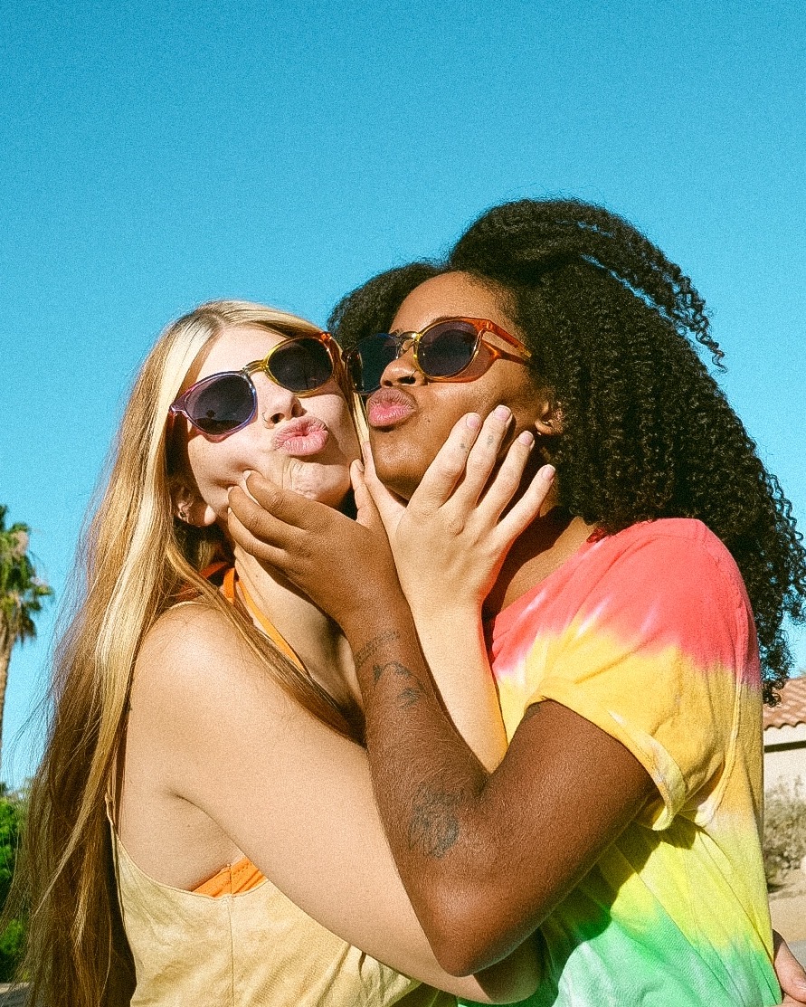 Two people wearing sunglasses and holding each other's faces