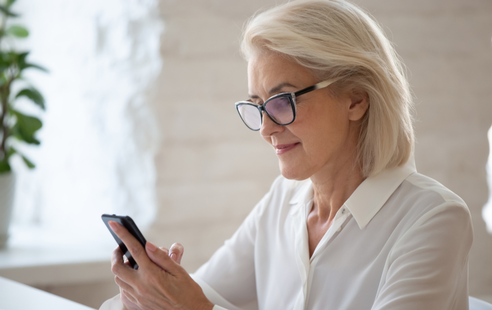 A woman wearing blue light filtering reading glasses looking at a phone